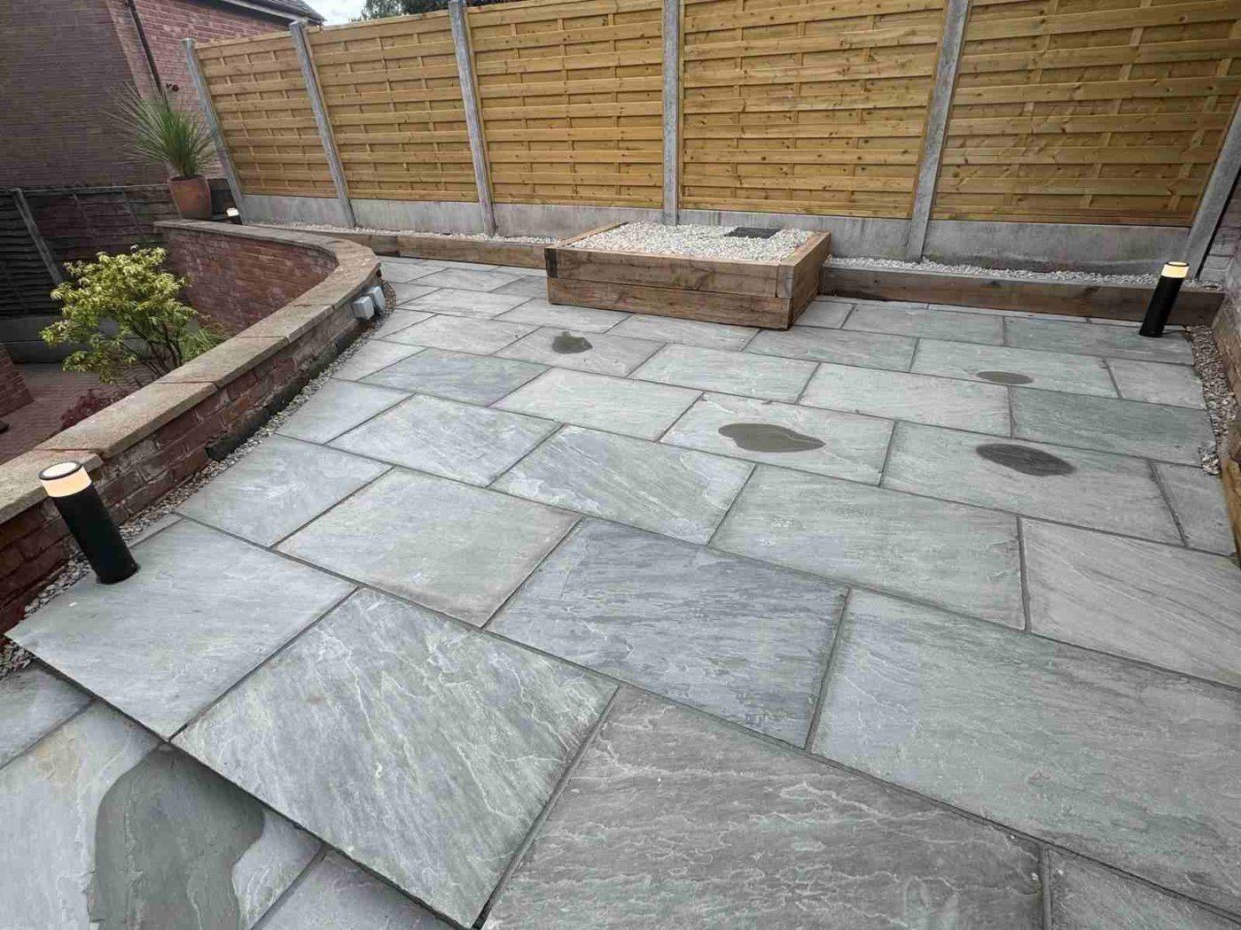 Upper tier of the new grey sandstone patio in Bramshall, near Uttoxeter, with a raised sleeper planter at the back