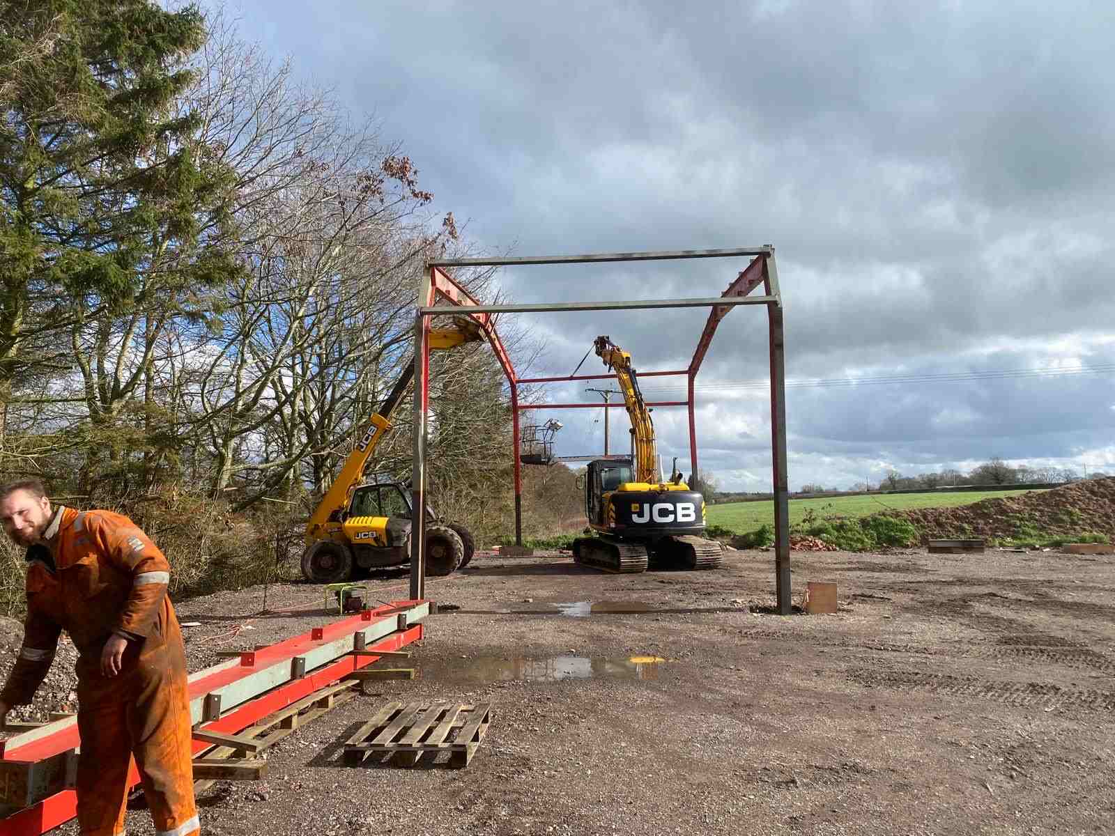 The first bay of a reused steel frame standing on a farm site near Penkridge, with steel members laid out ready