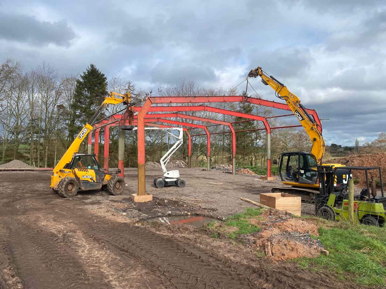 Steel portal frame of an agricultural building going up in Penkridge, with a JCB telehandler, excavator and cherry picker on site